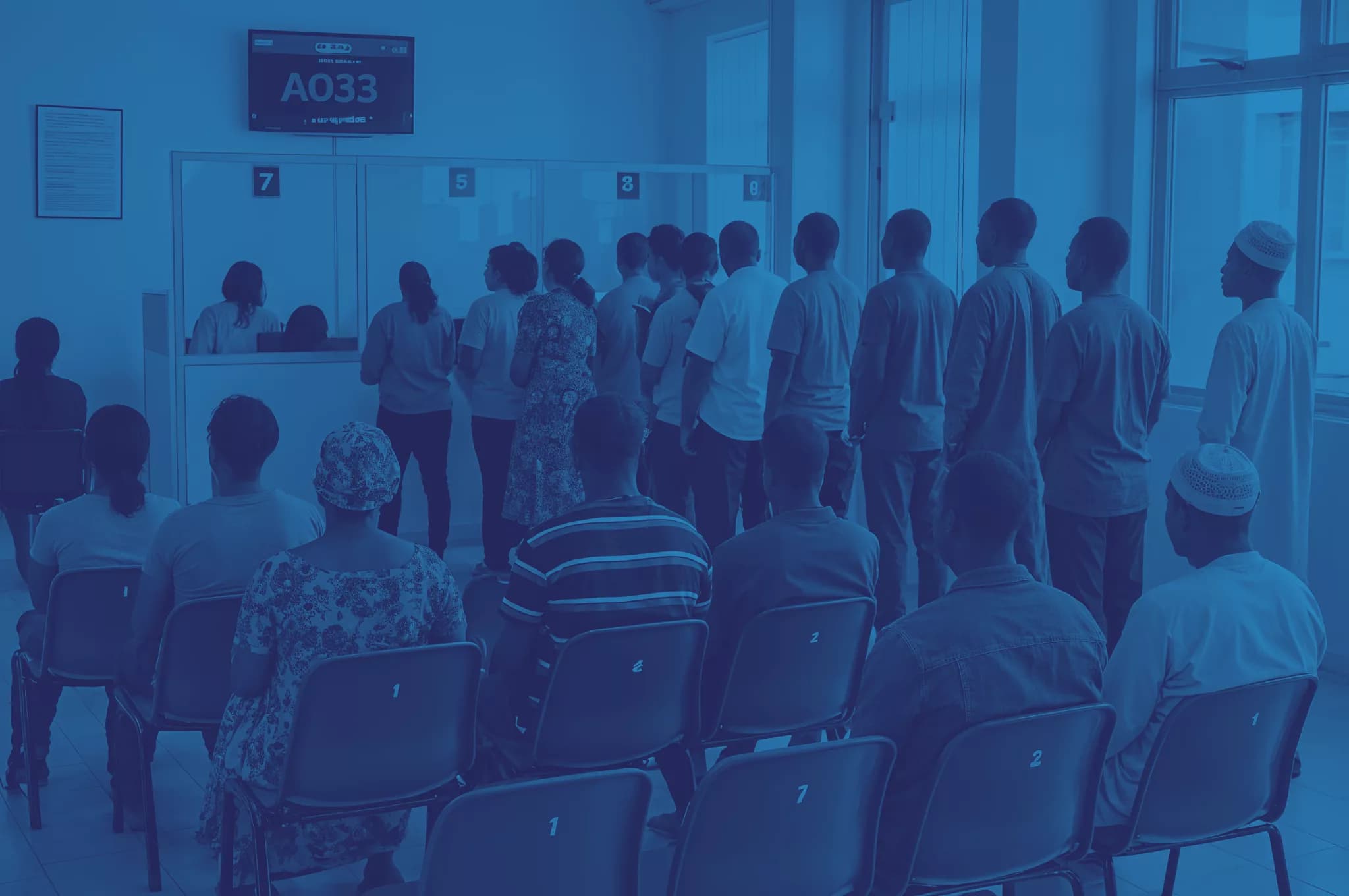 People waiting at numbered service counters beneath a queue display.